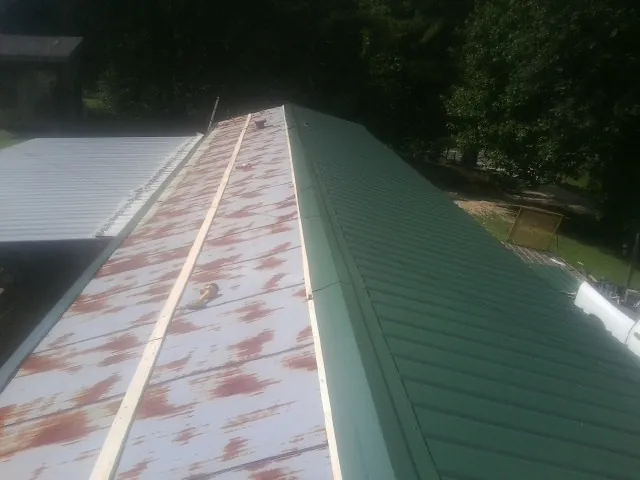 Old rusted panels beside newly installed green metal roofing — Wind Damage Roof Repair by Roofing Brothers in Dayton